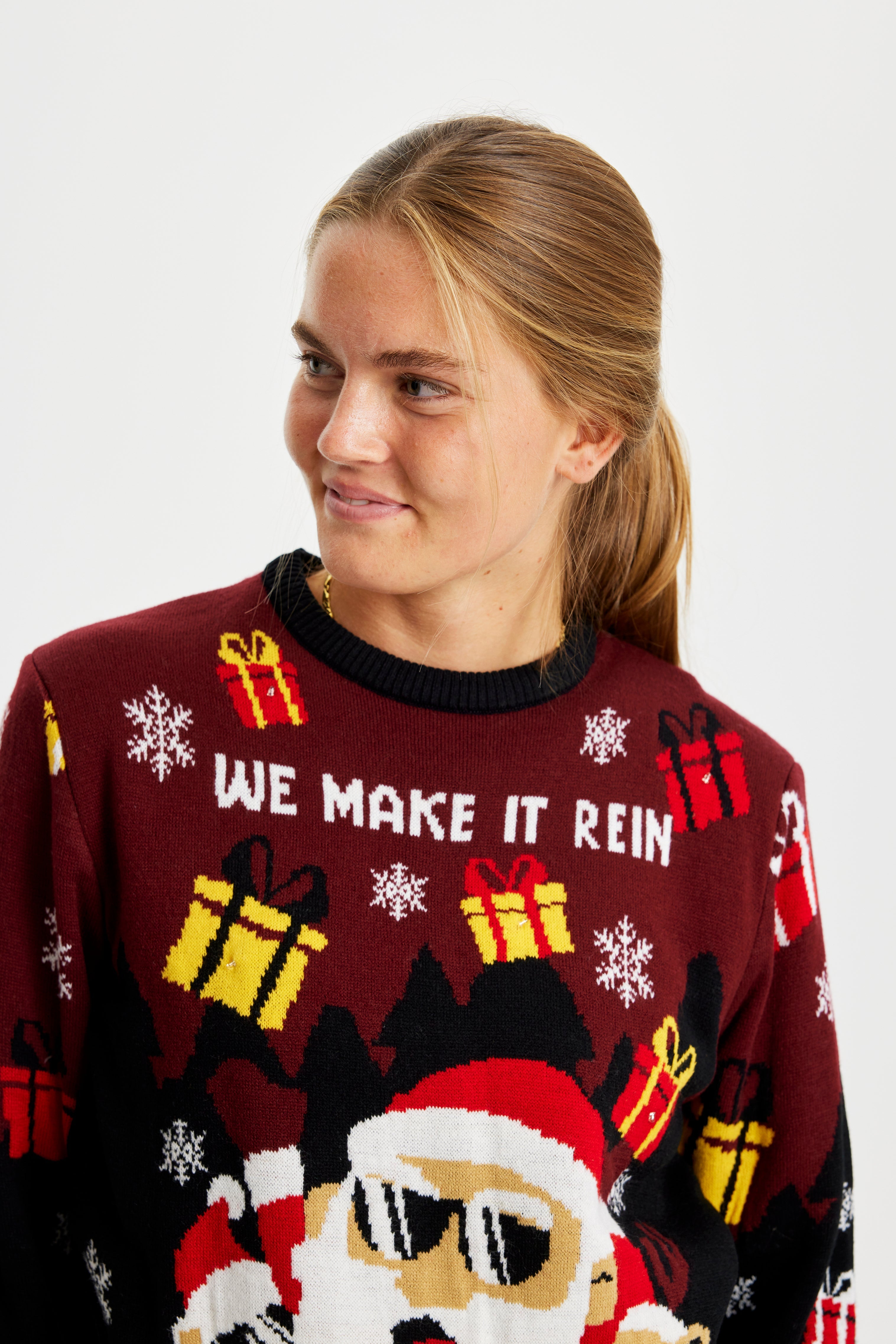 En kvinne poserer iført en selvlysende julegenser med gaver på.